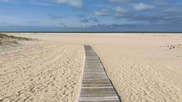 Pasarela de madera que conduce a una playa arenosa bajo un cielo despejado.