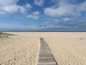 En träpromenad som leder till en sandstrand med en klar himmel.
