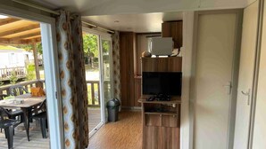 Una habitación con piso de madera, un televisor sobre un mueble de madera, una puerta y vista al exterior a través de un ventanal.