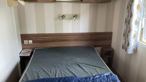 Un dormitorio con cama, cabecero de madera, repisa en la pared, mesita de noche y ventana con cortinas.