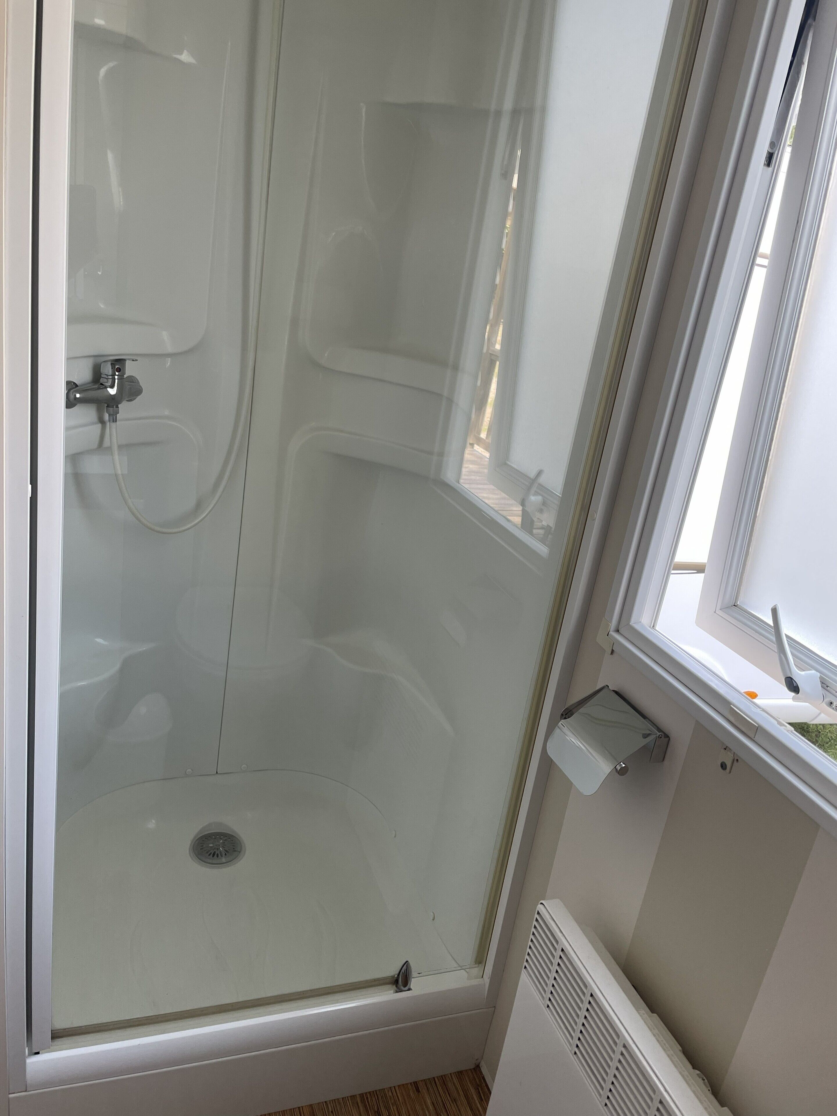 A glass-enclosed shower stall with a white exterior, a window to the right, and a small shelf below the window.
