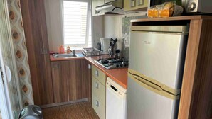Una cocina compacta con refrigerador, estufa, lavamanos y armarios de madera.