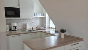 Pieni, käytännöllinen keittiö, jossa on valkoiset kaapit, mikroaaltouuni, kahvinkeitin ja pieni ruukkukasvi.