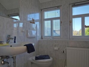 A bathroom with a white sink, a toilet, and a window with blinds. - Haus Küstenwind - Vacation for two on the top floor with 2 balconies - House (Wyk auf Föhr)