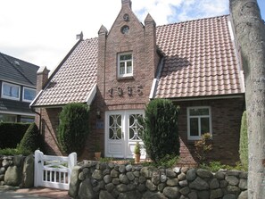 A traditional brick building with a tiled roof, a stone wall in front, and a white gate. - Haus Küstenwind - Vacation for two on the upper floor and 2 balconies - House (Wyk auf Föhr)
