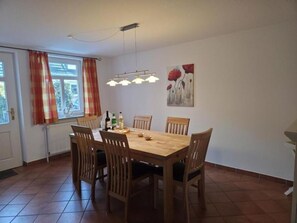 Ein Essbereich mit einem Holztisch und Stühlen, einem Gemälde an der Wand und einem Fenster mit Vorhängen.