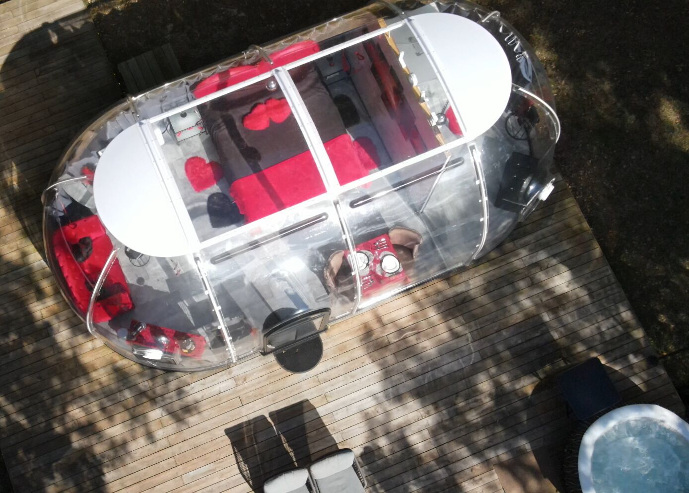 A transparent vehicle with red interior, parked on a wooden deck.