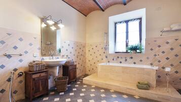 A bathroom with a large bathtub, a sink, a mirror, and a window.