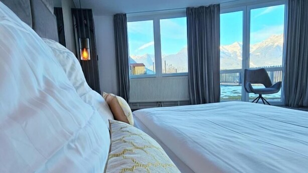 Een hotelkamer met een groot bed, een stoel bij het raam en uitzicht op bergen.