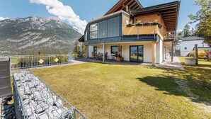 Een modern huis met twee verdiepingen, een balkon, een stenen muur en uitzicht op de bergen.