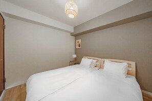 A neatly made bed in a room with a wooden headboard, a bedside lamp, and a framed picture on the wall. - E-US NAEBO 203 (Sapporo)
