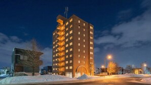A multi-story building with a central entrance and balconies, surrounded by snow and streetlights. - E-US NAEBO 203 (Sapporo)