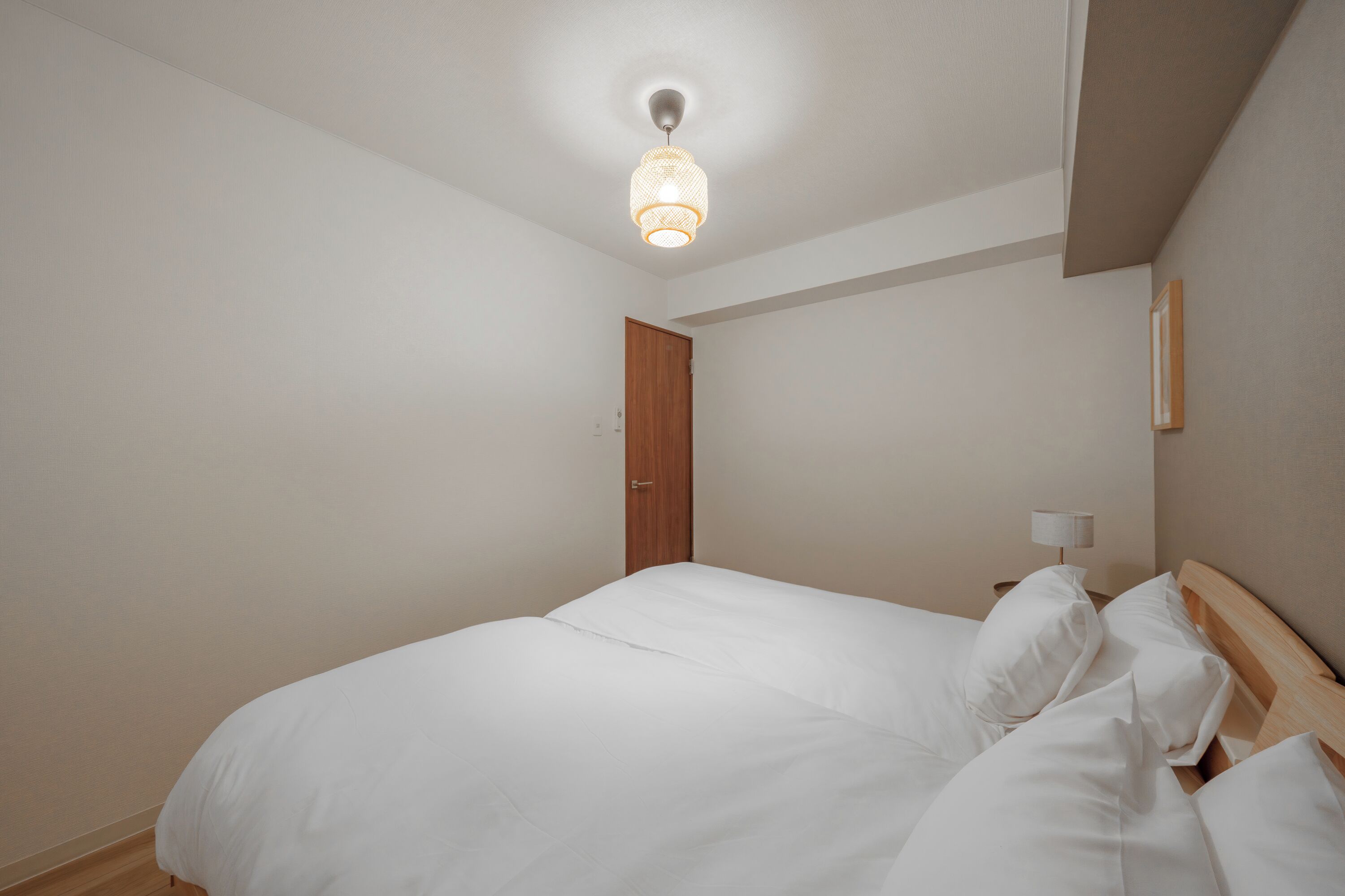 Een slaapkamer met een bed, een houten deur, een nachtkastje met een lamp en een plafondlamp.