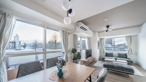 A modern living room with a wooden dining table, grey sofas, and a TV on a wooden stand. - E-US NAEBO 203 (Sapporo)