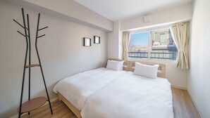 A modern hotel room with a large bed, a standing lamp, and a view of the city through the window. - E-US NAEBO 203 (Sapporo)