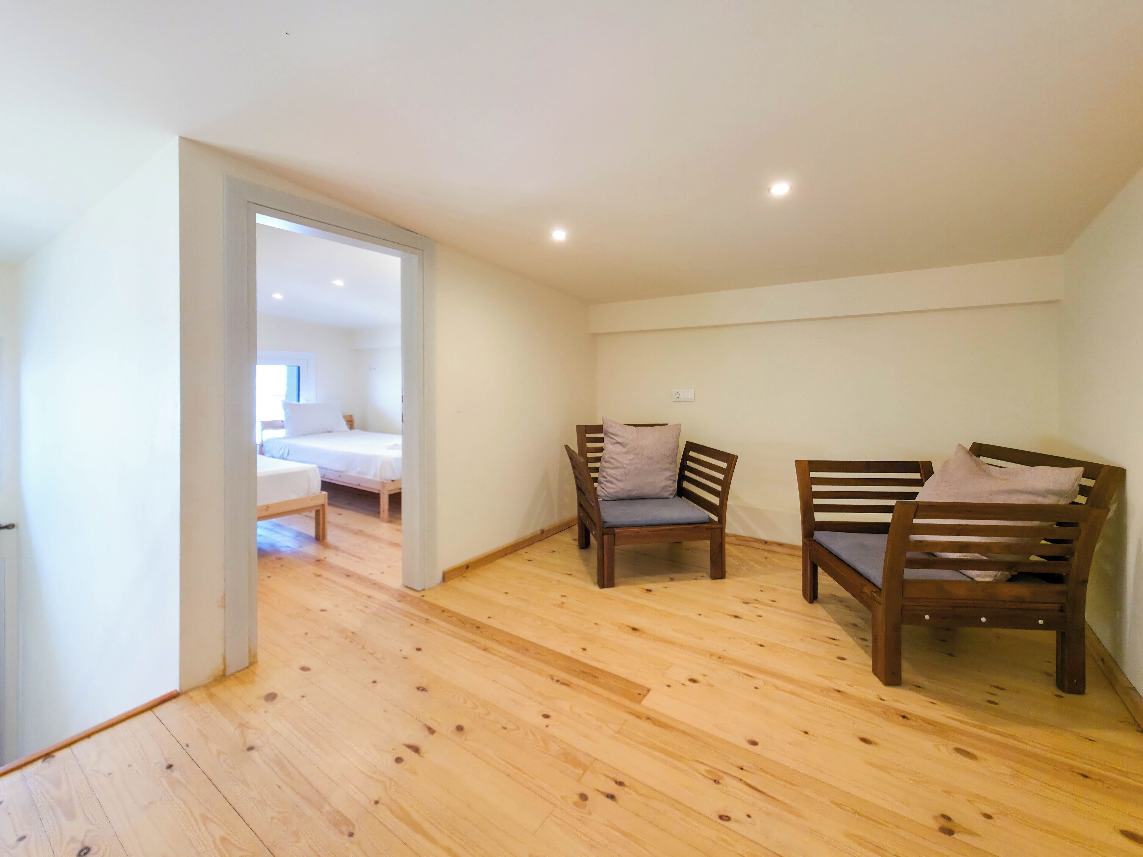 Una habitación con suelo de madera, dos sillas de madera, una cama y una puerta que da a otra habitación.