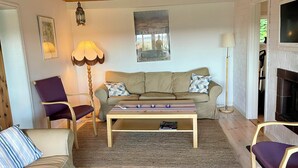 A cozy living room with a sofa, armchairs, a coffee table, and a fireplace. - Seaside plot with private jetty, rowing boat & sunset (Kvicksund)