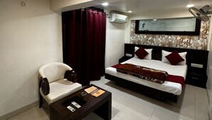A hotel room with a bed, a chair, a small table, an air conditioning unit, and a ceiling fan. - HOTEL BANJARA (Bhopal)