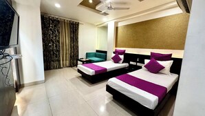 A hotel room with two beds, a ceiling fan, a TV, and a large window with curtains. - HOTEL BANJARA (Bhopal)