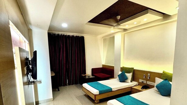 A hotel room with two beds, a TV, a desk, and a mirror. - HOTEL BANJARA (Bhopal)