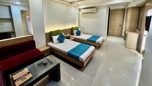 A hotel room with two beds, a red sofa, a glass coffee table, a ceiling fan, and an air conditioning unit. - HOTEL BANJARA (Bhopal)
