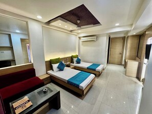 Habitación de hotel con dos camas, un sofá rojo, una mesa de centro de cristal, un ventilador de techo y un aire acondicionado.