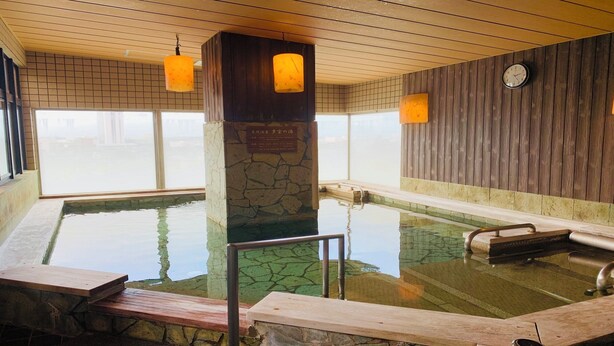 Een warmwaterbronbad met stenen zuilen, houten banken en een houten muur.