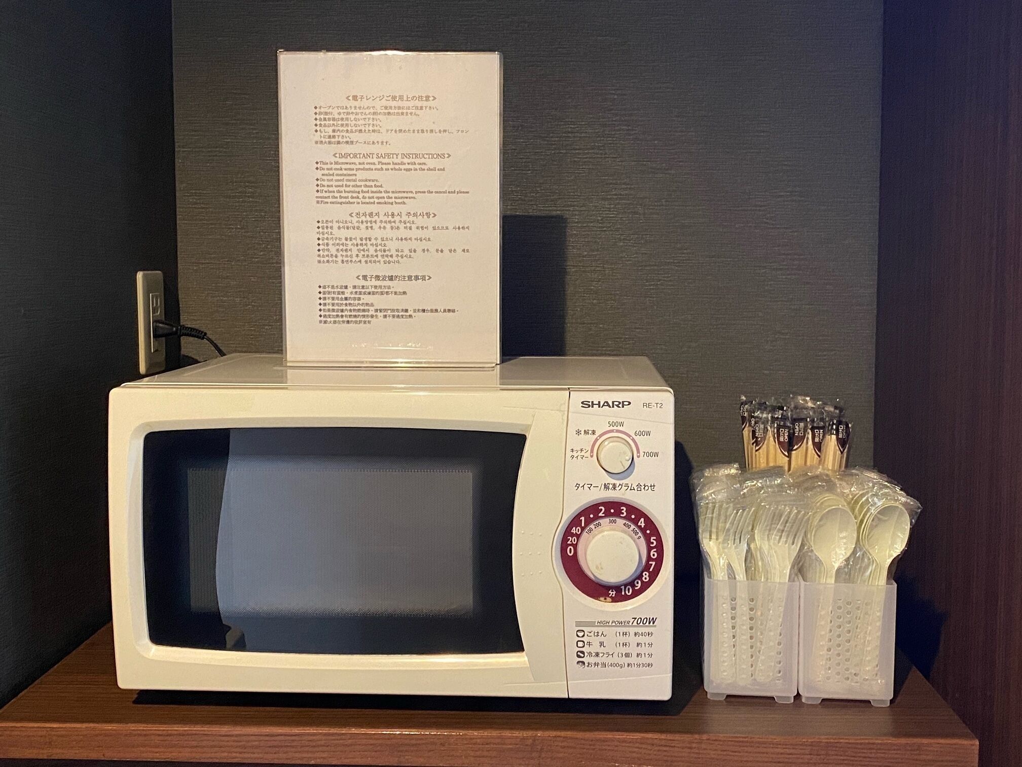 A Sharp microwave with a power dial, a plug, and a safety instruction sheet on top.