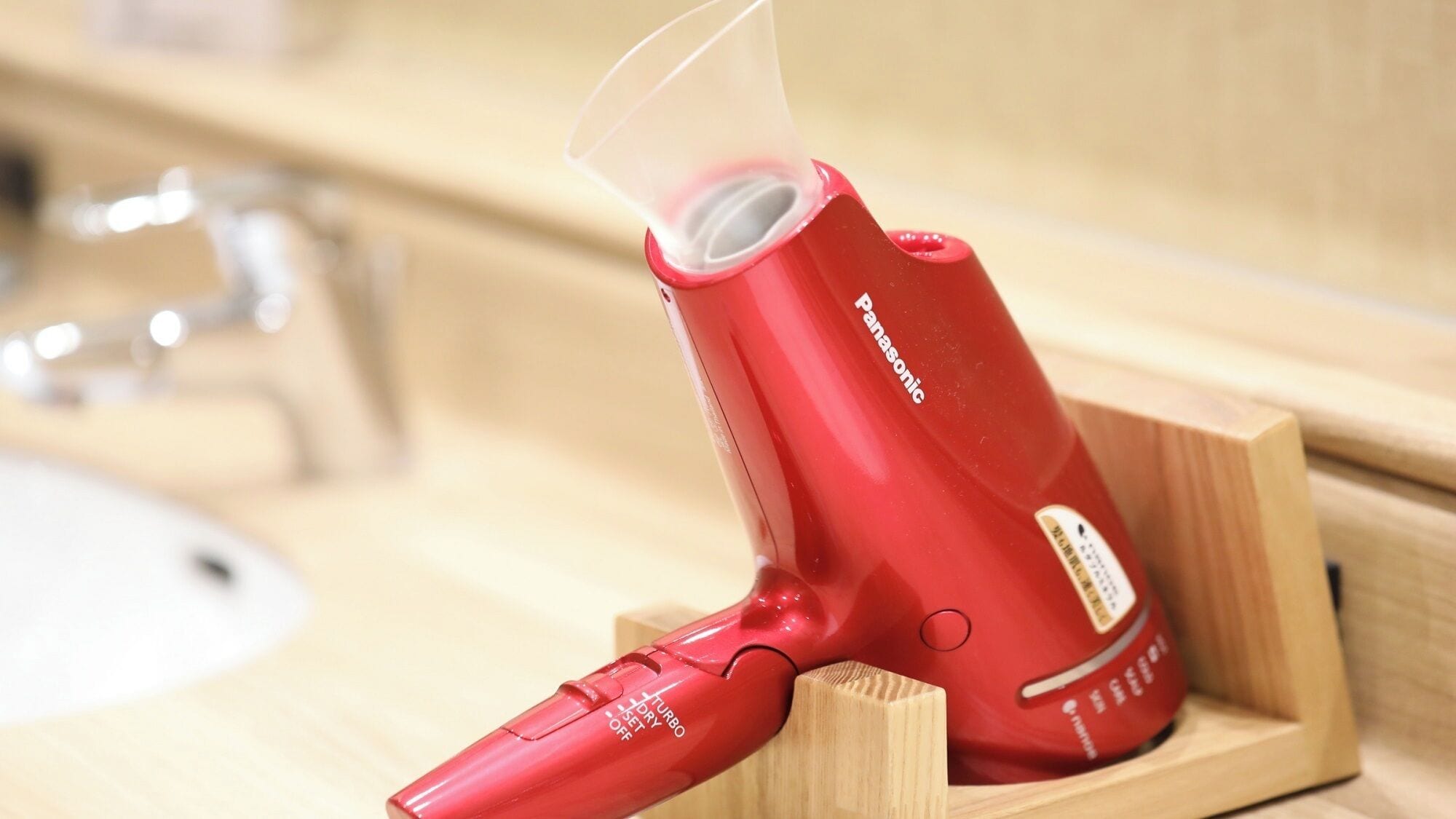 Un secador de pelo rojo Panasonic con boquilla transparente, sobre un soporte de madera.