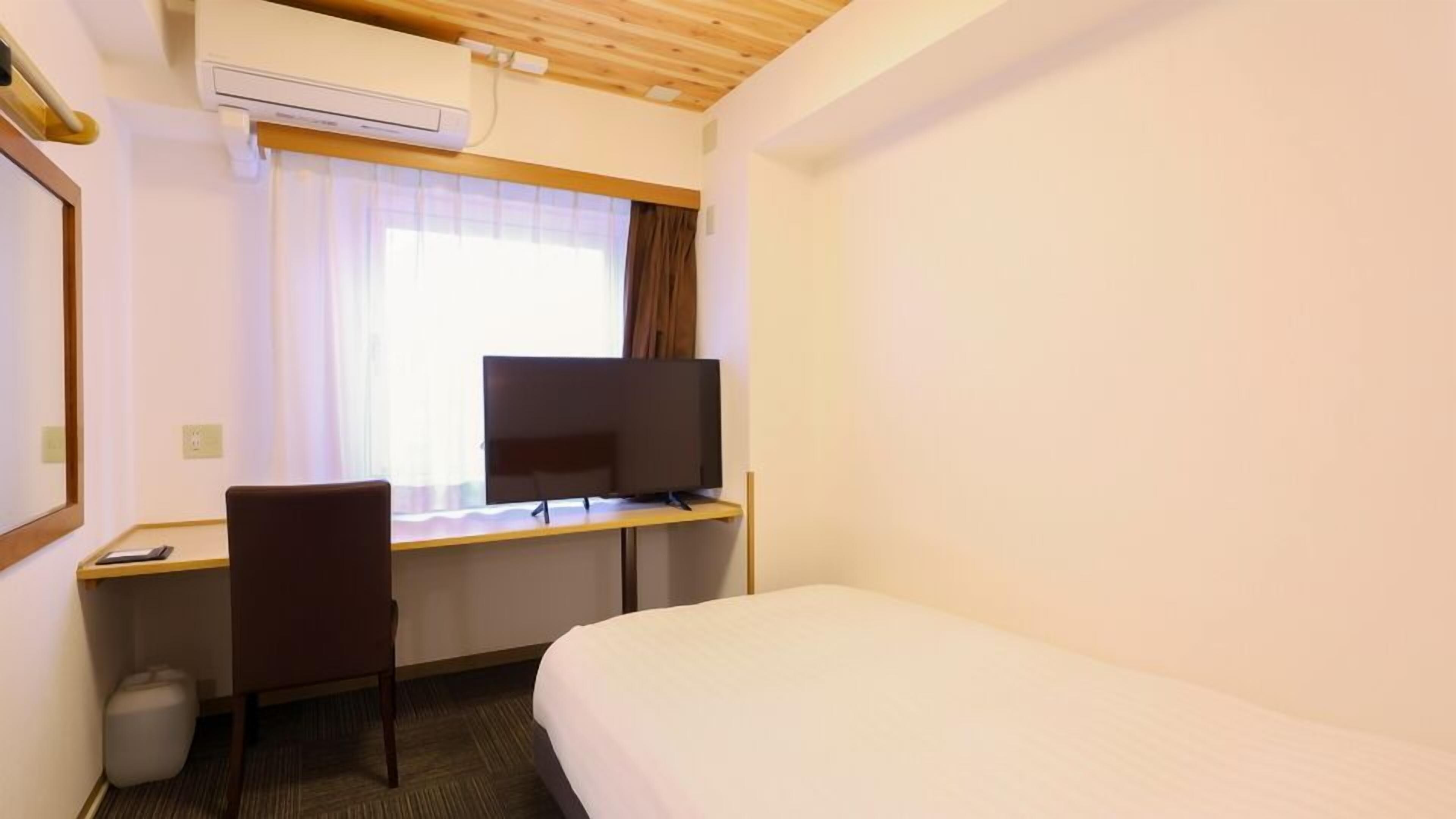 A hotel room with a bed, a desk with a computer, a chair, and a TV.