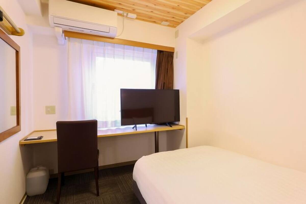 A hotel room with a bed, a desk with a computer, a chair, and a TV.