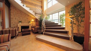 Een ruime woonkamer met een open haard, comfortabele zithoek, een trap en grote ramen.