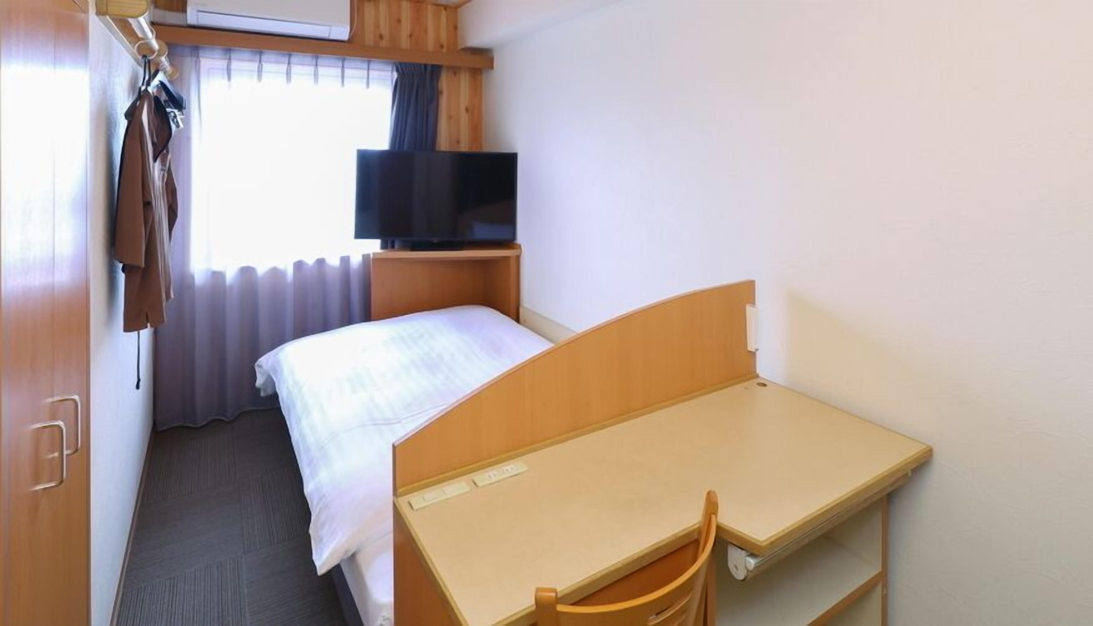 A hotel room with a bed, a desk, a chair, a television, and a window with curtains.
