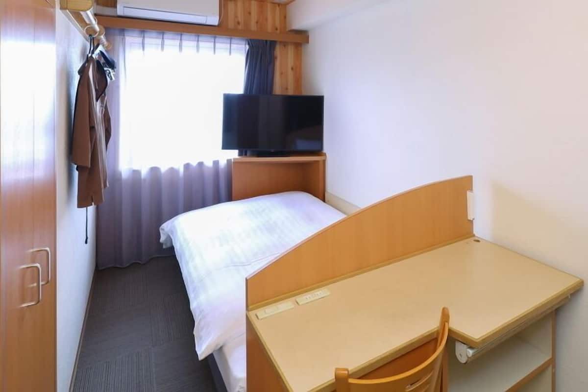 A hotel room with a bed, a desk, a chair, a television, and a window with curtains.