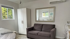 Una camera da letto con un letto, un divano grigio, un armadio, uno specchio e una finestra con vista su del verde.