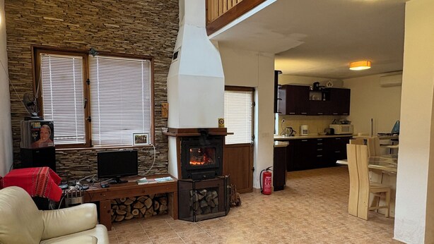 A living room with a fireplace, a television, and a dining area with wooden chairs.
