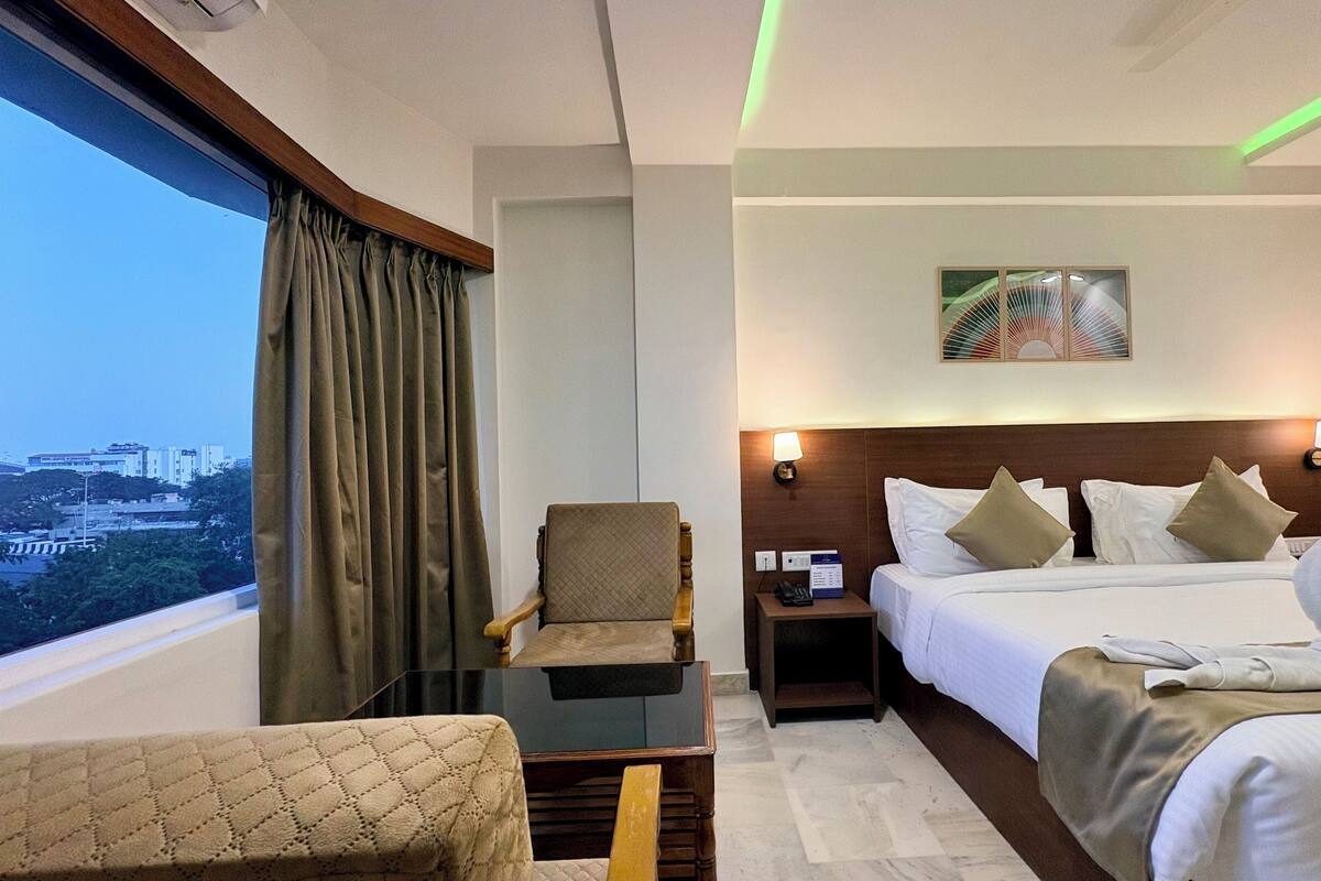 Une chambre d’hôtel avec un lit, une chaise, une table de chevet et une fenêtre avec des rideaux.