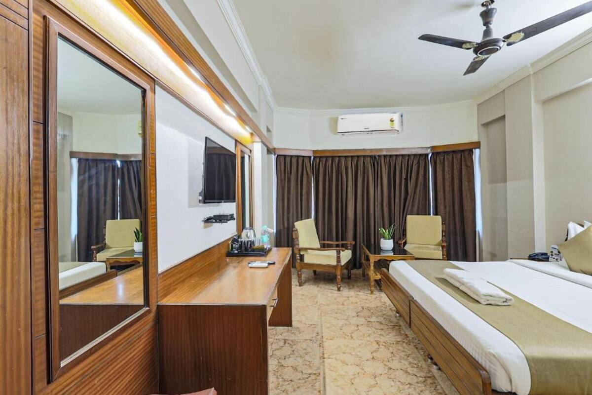 Une chambre d’hôtel équipée d’un lit, d’un bureau, d’une chaise, d’un miroir et d’un ventilateur de plafond.