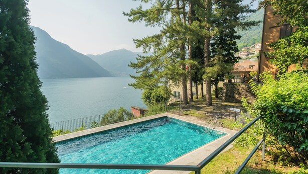 Une piscine rectangulaire à l’eau d’un bleu limpide, entourée d’une rambarde métallique. Au fond, on aperçoit un lac et des montagnes.