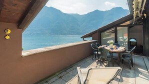 Un balcon avec une table et des chaises, donnant sur un lac et des montagnes.