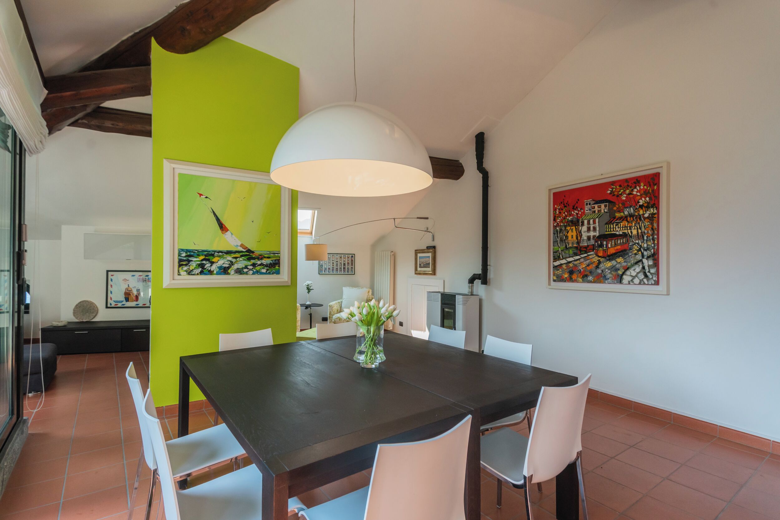 A dining area with a dark wooden table, white chairs, a vase with flowers, and artwork on the walls.