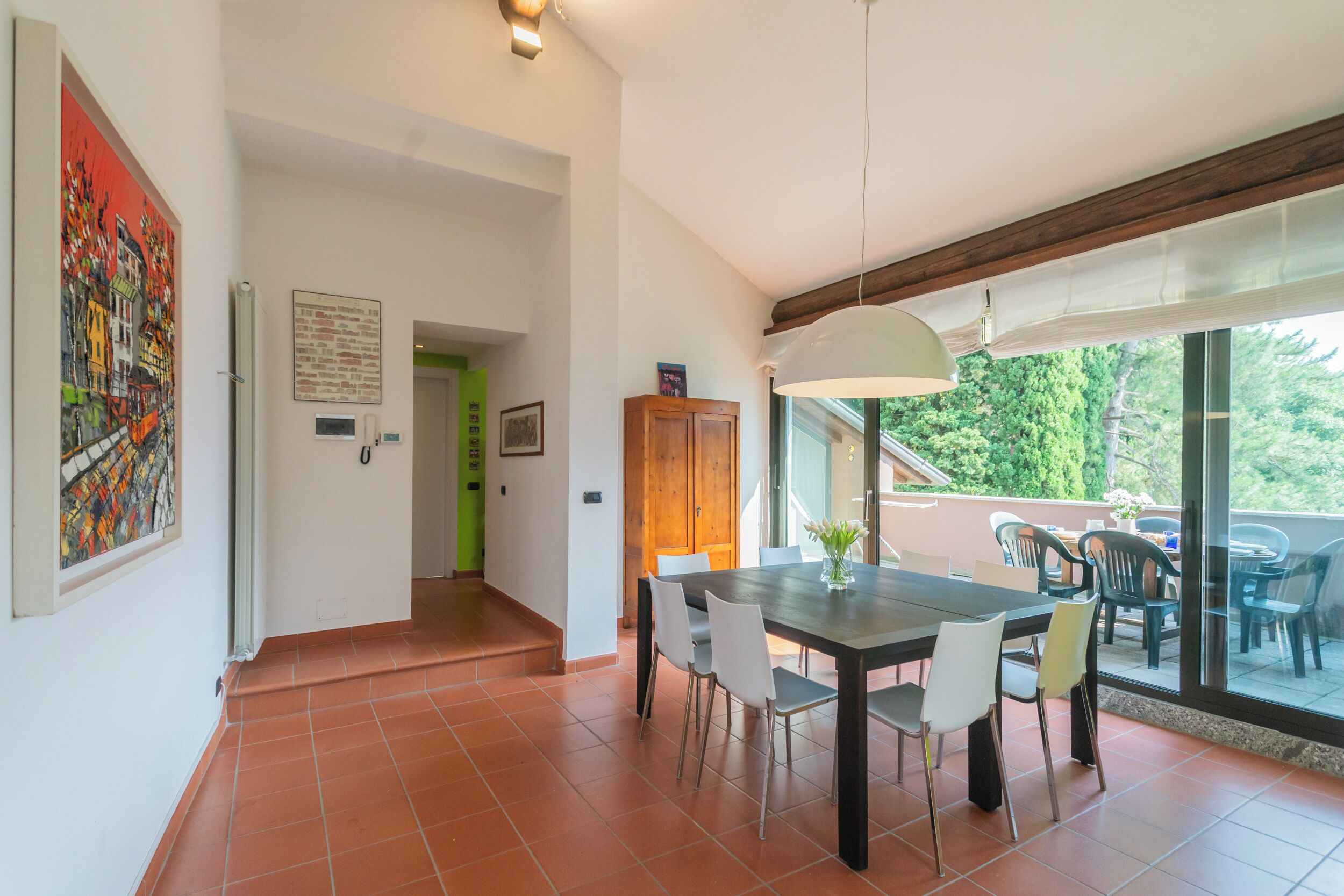Un comedor con una mesa grande y sillas, un lámpara colgante, y vista a un patio exterior a través de un ventanal.