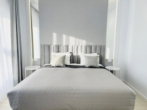 Un dormitorio moderno con una cama grande, dos mesitas de noche y una paleta de colores neutros.