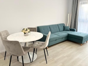 Una sala de estar moderna con un sofá seccional color turquesa, una mesa redonda de comedor con dos sillas, y un jarrón con flores.