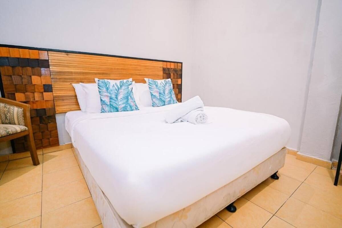 Una cama bien hecha con ropa blanca, un cabecero de madera con diseño de ladrillo y una silla con cojín.