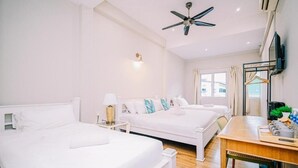 Habitación de hotel con dos camas, ventilador de techo, escritorio con silla, televisor y ventana con cortinas.