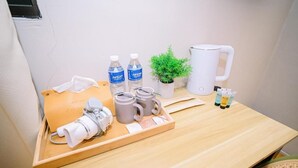 Una mesa de madera con una bandeja que contiene artículos de aseo, una planta en maceta, una taza blanca y botellas de agua.