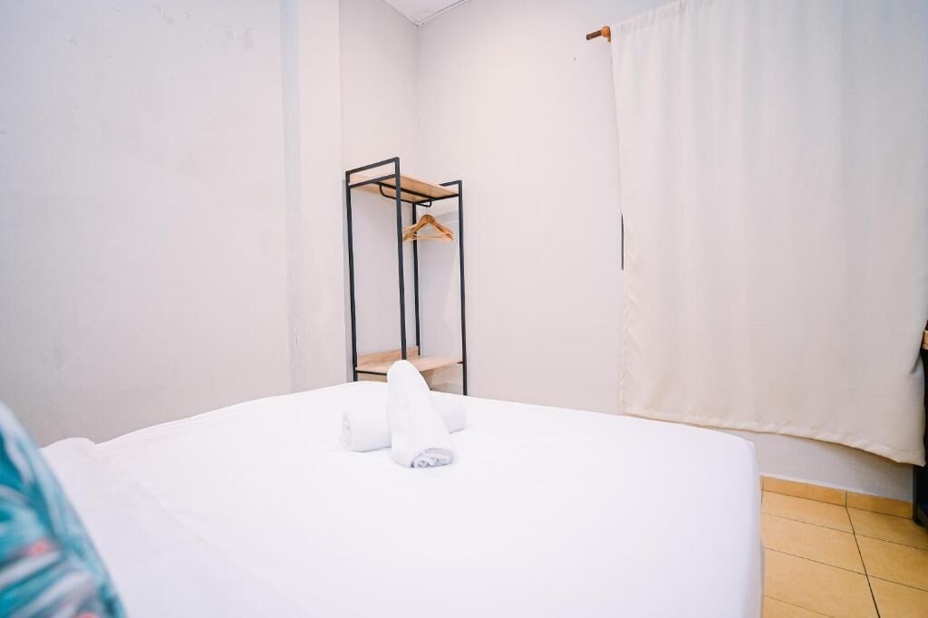 A hotel room with a bed, a wooden hanger shelf, and a white curtain.