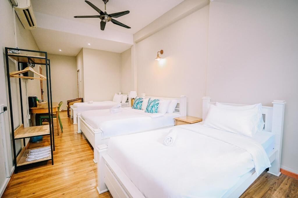 Habitació d'hotel amb dos llits, un ventilador de sostre, una làmpada penjada a la paret i un terra de fusta.