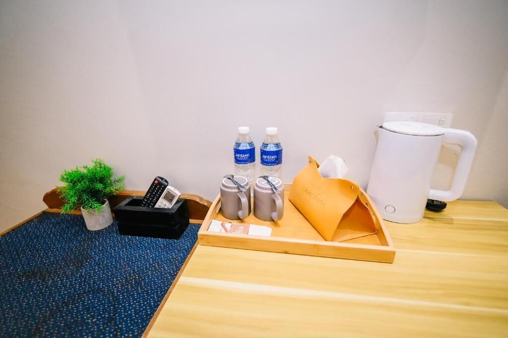A hotel room with a wooden table, a tray with water bottles, a coffee maker, a remote control, a small plant, and a black phone stand.